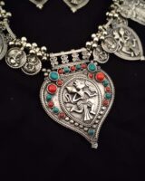 Intricate silver jewelry necklace featuring Lord Vishnu motif with colorful red and turquoise beads, showcasing traditional Indian craftsmanship and ethnic style.