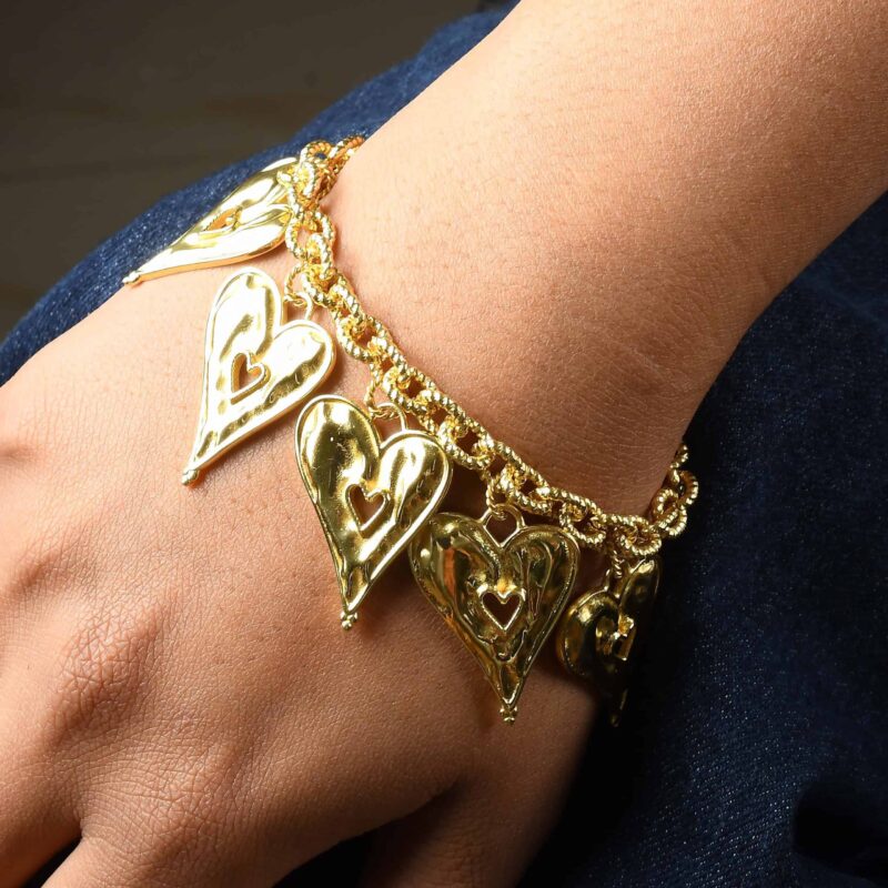 Gold heart-shaped jewelry bracelet with intricate cut-out details and chain links, styled on a wrist against a dark background, highlighting elegant Indian fashion jewelry.