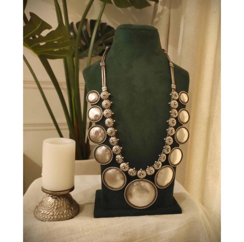 Shimmering silver statement necklace with large circular and floral design elements, perfect for Indian fashion jewelry.