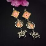 Colorful traditional Indian jewelry earrings featuring hand-painted floral motifs, goddess figures, and silver cow charms, ideal for festive attire and cultural celebrations.