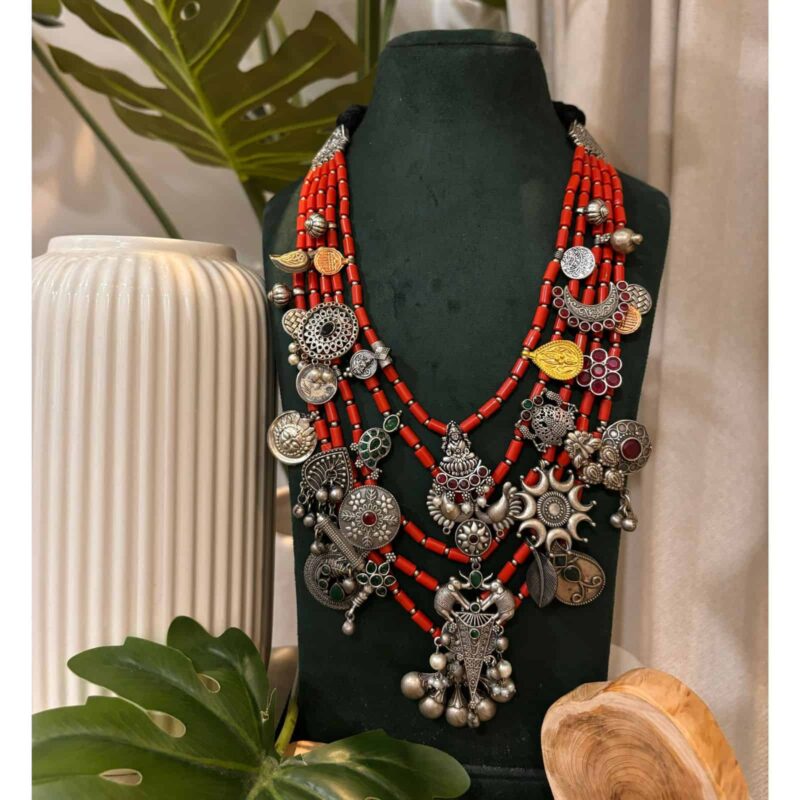 Colorful Indian traditional jewelry with red beads and silver charms on black display bust, showcasing handcrafted ethnic necklace design perfect for Indian fashion jewelry lovers.