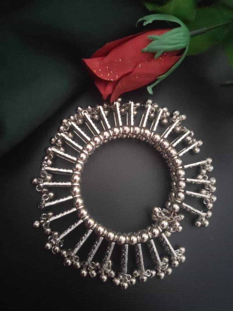 Shiny silver traditional Indian jewelry bracelet with intricate design, placed next to a vibrant red rose on black background for elegant jewelry showcase.
