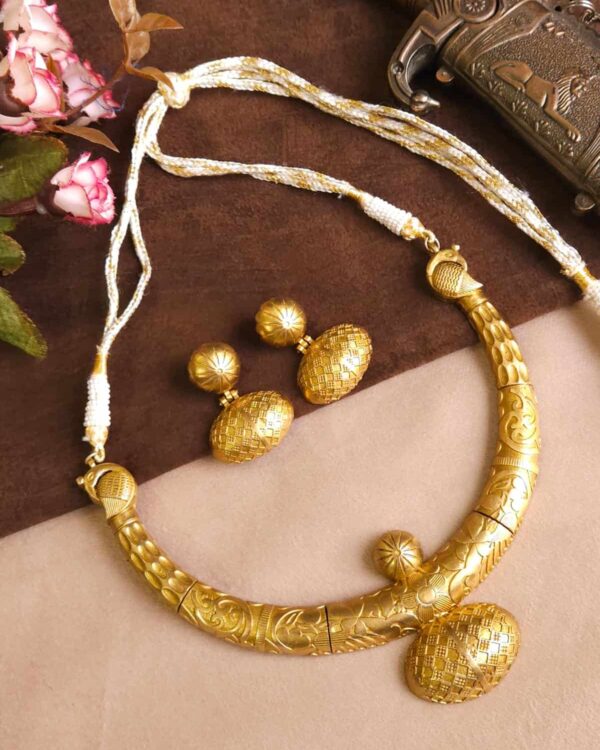 Golden traditional Indian jewelry necklace with intricate designs and matching earrings on a fabric background.