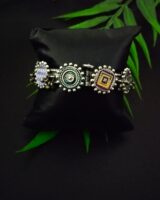 Intricate Indian traditional silver jewelry bracelet with colorful enamel accents, displayed on a black cushion with green leaves, ideal for ethnic fashion and cultural accessorizing.
