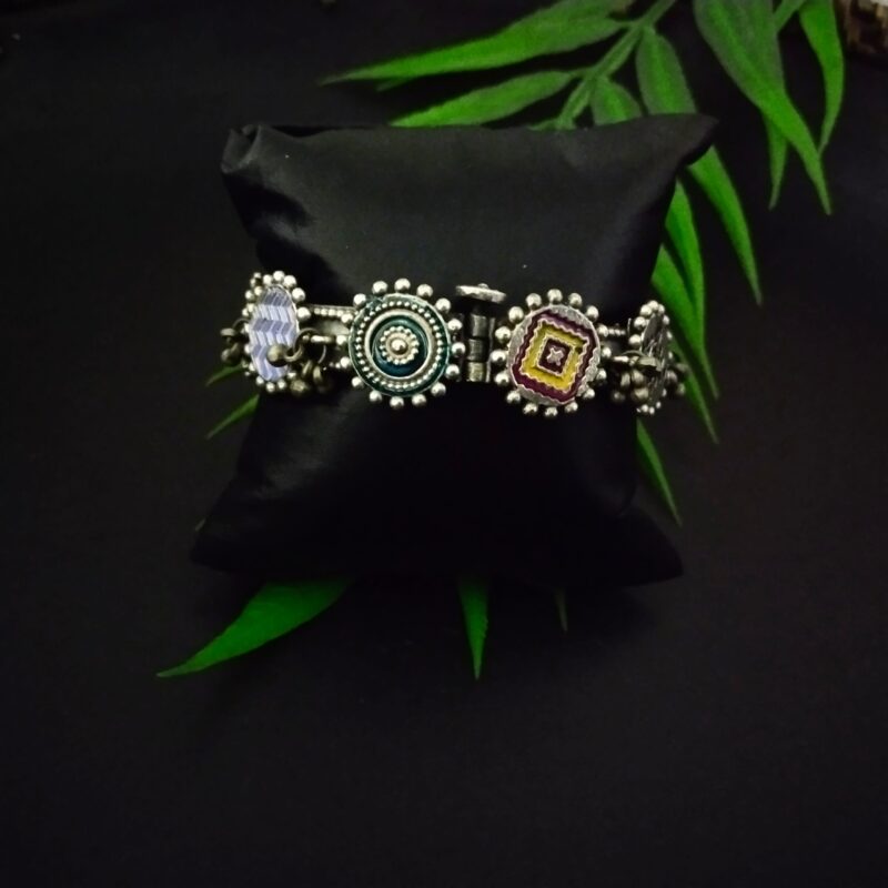 Intricate Indian traditional silver jewelry bracelet with colorful enamel accents, displayed on a black cushion with green leaves, ideal for ethnic fashion and cultural accessorizing.