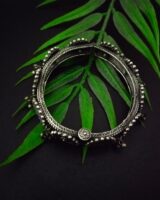 Vintage Indian tribal silver jewelry bracelet with intricate design, surrounded by lush green fern leaves, perfect for traditional fashion accessories and ethnic jewelry collections.
