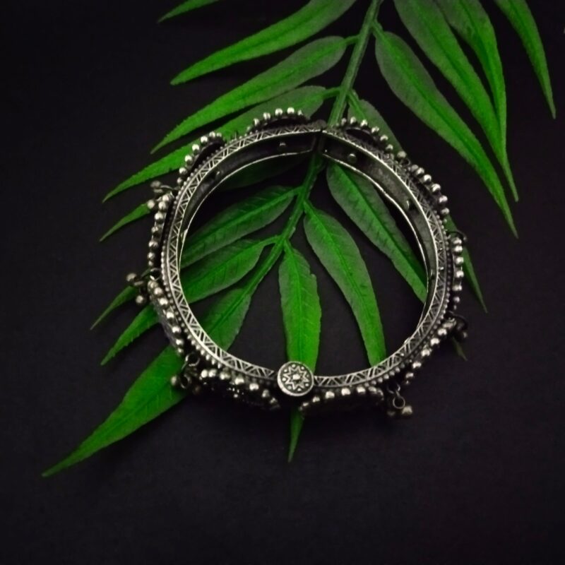 Vintage Indian tribal silver jewelry bracelet with intricate design, surrounded by lush green fern leaves, perfect for traditional fashion accessories and ethnic jewelry collections.