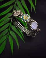 Intricate Indian boho silver bracelet featuring colorful enamel and geometric designs, showcased on a green fern leaf against a black background, highlighting traditional ethnic jewelry craftsmanship.