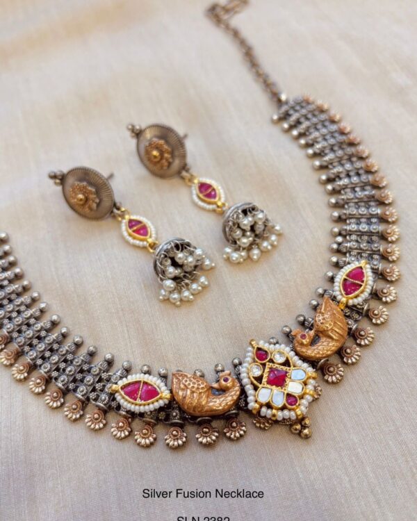 Intricate silver fusion necklace with peacock and floral motifs, embedded pink and white stones, paired with matching traditional earrings, perfect for Indian jewelry and ethnic wear.