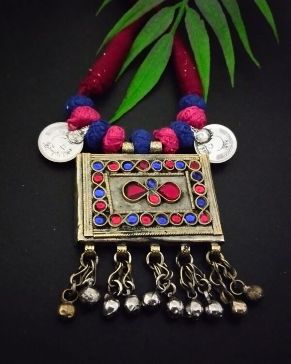 Colorful traditional Indian jewelry necklace with red, blue, and pink beads, metallic pendant with intricate design, hanging silver bells, and coin accents, perfect for ethnic fashion and festivities.