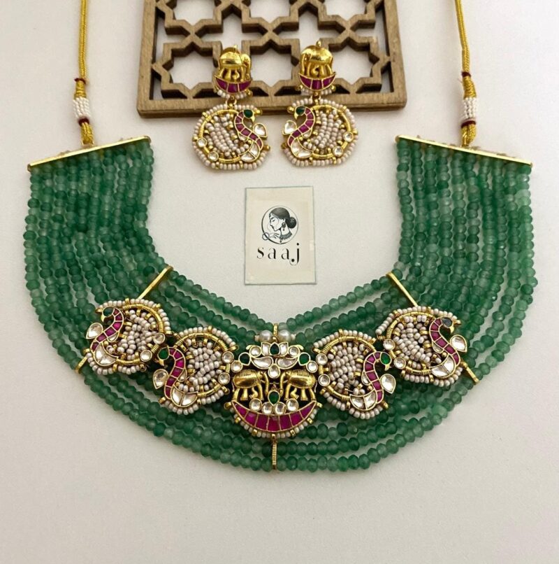 1550 Elegant green beaded Indian jewelry set with gold-toned, pearl, and ruby accents, including necklace and earrings, perfect for traditional occasions and festive celebrations.