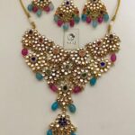 Elegant Indian jewelry set with gold-plated necklace and matching earrings featuring colorful stones, pearls, and intricate floral design. Perfect for traditional occasions and festivals.