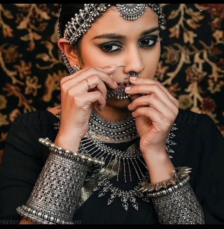 Intricate traditional Indian jewelry set featuring silver necklaces, bangles, earrings, and a nose ring, paired with elegant attire for cultural or festive occasions.