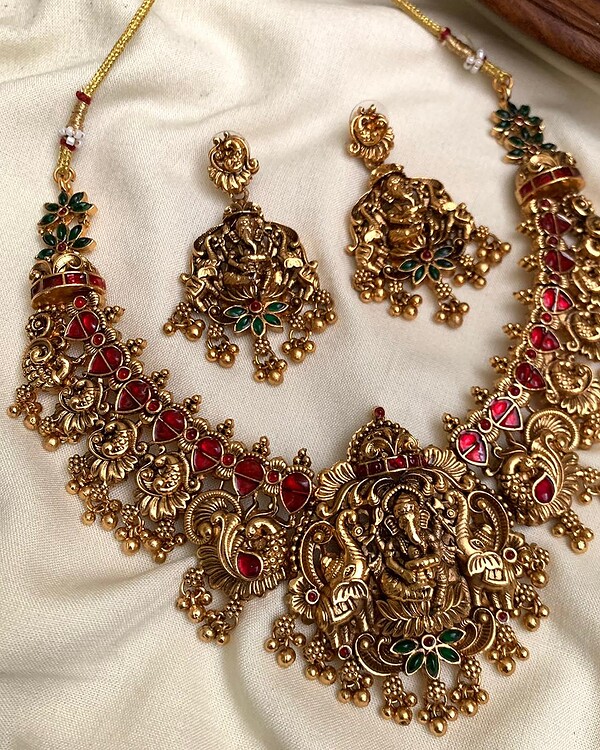 Exquisite gold-plated Indian jewelry set with traditional pendant necklace and matching earrings adorned with red and green gemstones, perfect for festive and special occasions.