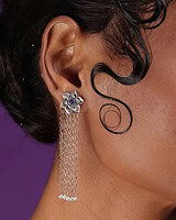 Elegant silver floral earrings with dangling chains and blue gemstone center on a woman's ear, showcasing traditional Indian jewelry style.