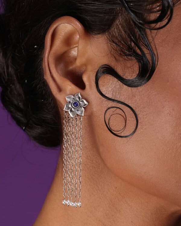 Elegant silver floral earrings with dangling chains and blue gemstone center on a woman's ear, showcasing traditional Indian jewelry style.