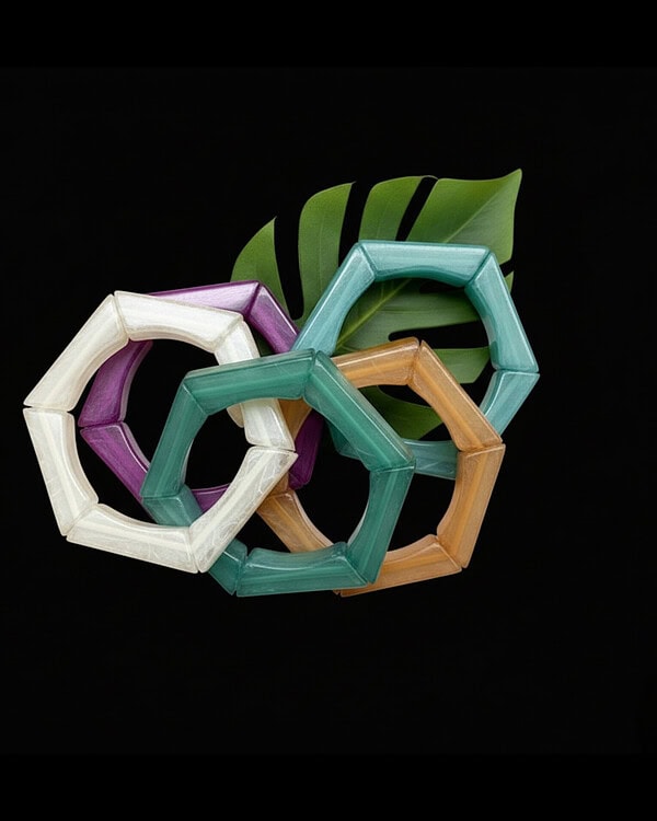 Colorful geometric bangles made of eco-friendly resin displayed with green tropical leaves on a black background. Stylish Indian fashion jewelry ideal for festive and modern accessories.