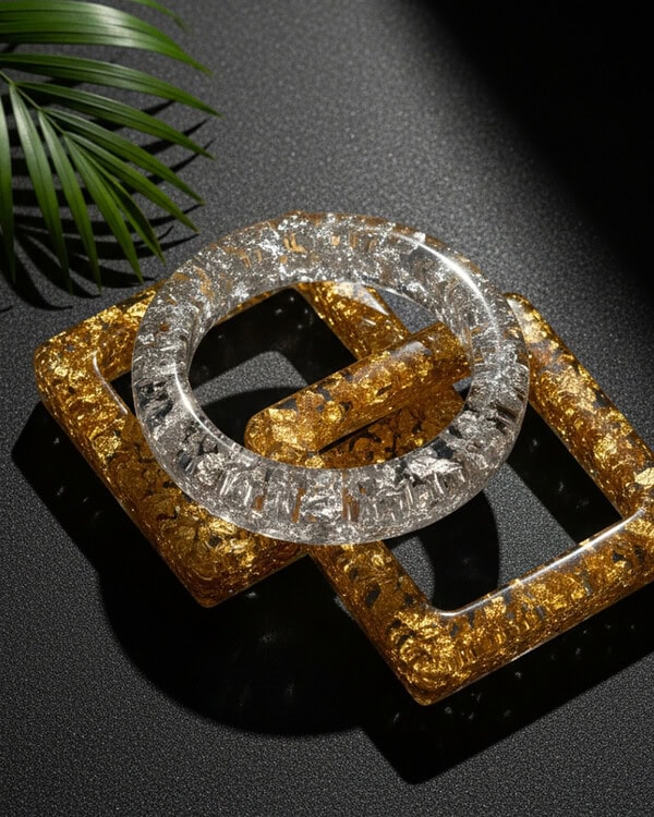 Shimmering acrylic bangles in silver and gold tones with textured designs, perfect for ethnic Indian jewelry looks, displayed on a black surface with a green leaf accent.