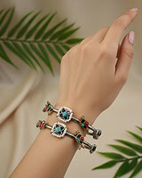 Hand wearing traditional Indian silver bangles with colorful inlay accents and intricate design, styled with a neutral background and green leaves to showcase elegant jewelry.