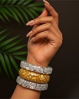 Vibrant Indian fashion jewelry bangles on a stylish hand against a dark background with green leaves, showcasing a mix of silver and gold-toned accessories perfect for traditional or contemporary wear.