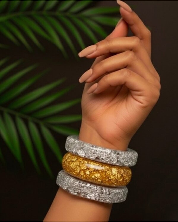 Vibrant Indian fashion jewelry bangles on a stylish hand against a dark background with green leaves, showcasing a mix of silver and gold-toned accessories perfect for traditional or contemporary wear.