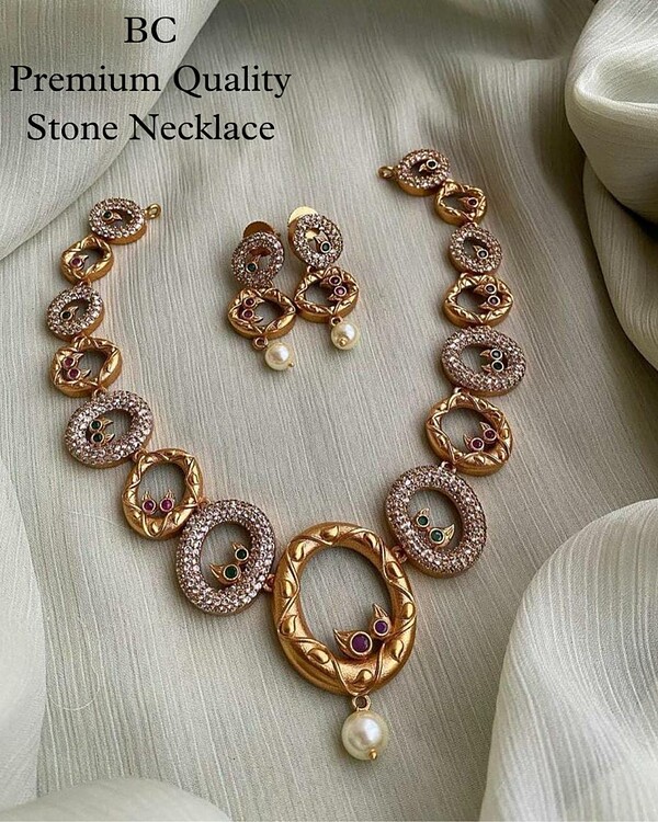 Elegant Indian gold-plated jewelry set featuring a statement necklace and matching earrings with intricate designs, sparkling stones, and pearl accents, perfect for traditional occasions.