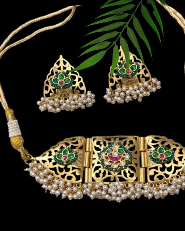 Intricate gold jewelry set with pearl embellishments, featuring traditional earrings and a choker necklace with green and pink gemstone accents, perfect for Indian festive occasions.