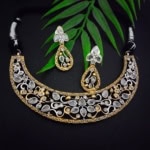 Jewelry set including necklace and earrings with black and gold detailing, adorned with white stones, showcased on a black background with a green leaf for a sophisticated, Indian fashion jewelry look.